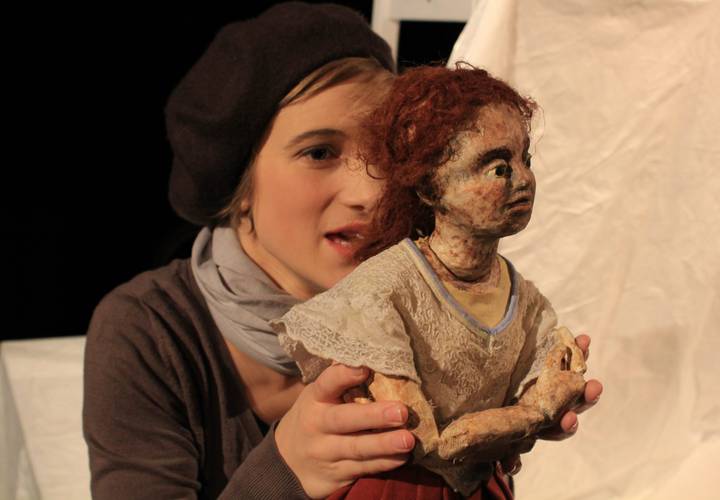 Die Schneekönigin – Person mit dunkler Mütze und Schal hält eine Puppe mit roten Haaren und ausdrucksvollem Gesicht. Hintergrund ist unscharf und hell.