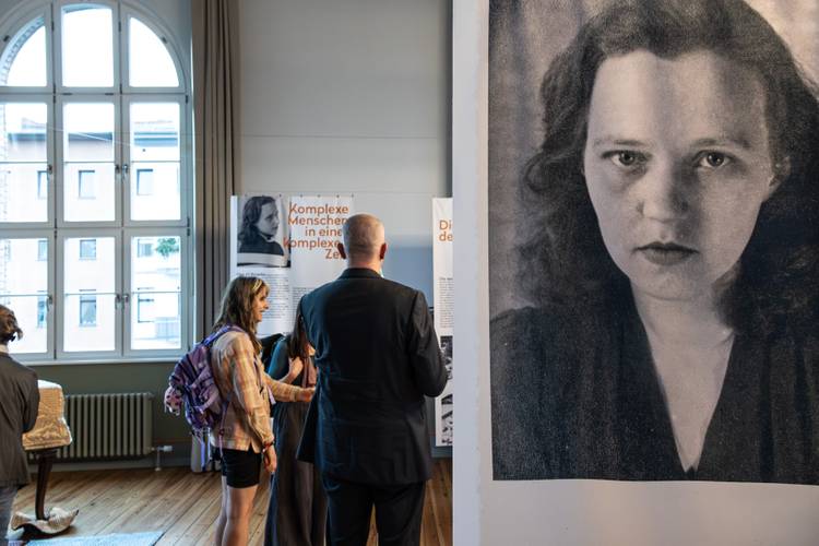 Blick in die Ausstellung "Lang ist es nicht her. Und jetzt ist es soweit." – Ein Panel mit Portraitaufnahme der Schriftstellerin Susanne Kerckhoff, im Hintergrund Besuchende in der Ausstellung.