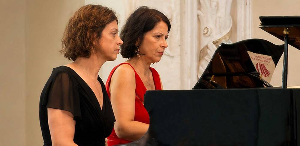 Maria-Magdalena Pitu-Jokisch und Beatrice Wehner-Schaller (Klavier) – Zwei weiblich gelesene Personen spielen zu zweit an einem Klavier. Eine trägt ein schwarzes, die andere ein rotes Kleid.