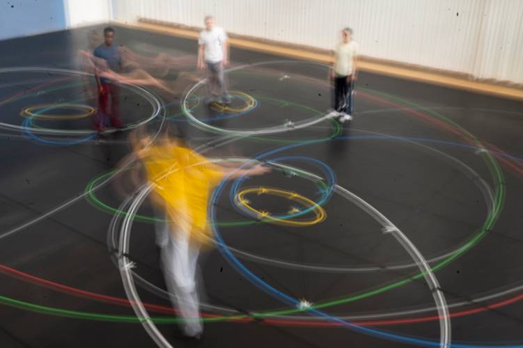 Gla55. 10 movements to the music of Philip Glass – Mehrere Personen stehen oder bewegen sich in einem Probenraum, um sie herum sind bunte Kreise.