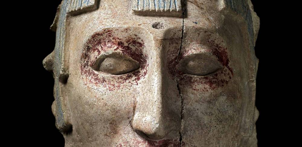 Stuckkopf (Fälschung), Mexiko, Detail, Datierung unbekannt, Gips – Nahaufnahme einer antiken Skulptur eines Gesichts mit dunklen Markierungen um die Augen. Mittiger Riss im Stein. Kunstwerk aus Stein, Detailaufnahme.