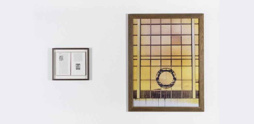 Sophie Calle, The Detachment, 1996, Farbfotografie und Buch, 2-teilig, 120 x 90 x 4 cm (Bild) – Ein kleines gerahmtes Dokument links und ein großes Foto eines Fensters mit gelbem Licht und kreisförmigem Metallmuster rechts, beide an einer weißen Wand.