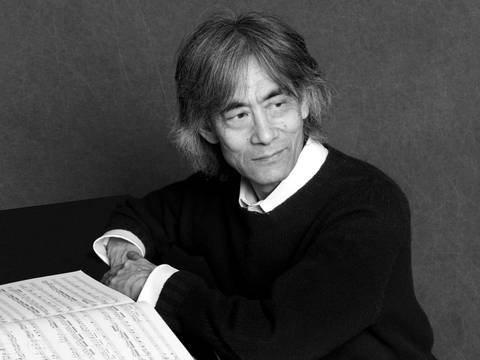 Kent Nagano – Ein älterer Mann mit grauen Haaren sitzt vor einer aufgeschlagenen Partitur und schaut nachdenklich an der Kamera vorbei.