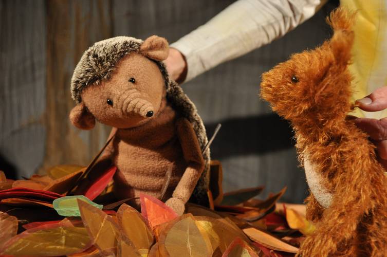 Herr Eichhorn und der erste Schnee – Zwei Stofftiere, ein Igel und ein Eichhörnchen, stehen in einem Haufen bunter Blätter. Hände einer Person halten die Puppen.