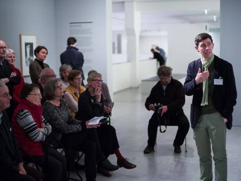 Zirkeltraining in der Berlinischen Galerie – Foto: Viele Menschen stehen und sitzen im Ausstellungsraum und schauen auf eine Person, die spricht und auf ein Gemälde deutet.