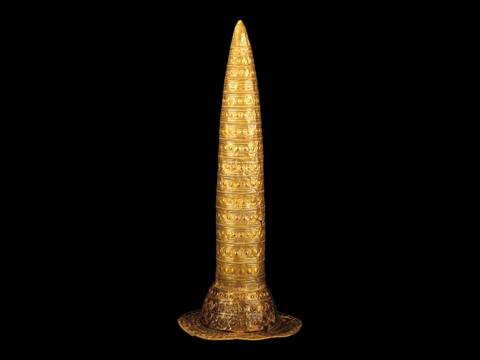 Den Berliner Goldhut zieren verschiedene Kreisornamente, die als lunisolarer, d.h. auf Sonne und Mond basierenden Kalender verstanden werden können. Sie stehen für die Verbindung von Kult, Wissen und auch materiellem Reichtum. – Goldener, verzierter konischer Helm auf schwarzem Hintergrund. Kunstwerk mit kreisförmigen Mustern in parallel verlaufenden Reihen.