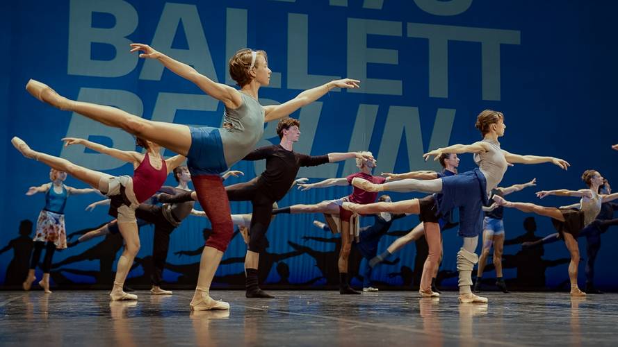 Training zum Zuschauen – Mehrere Personen beim Balletttraining stehen in einer Linie auf einem Bein. Hintergrundtext: Ballett Berlin.