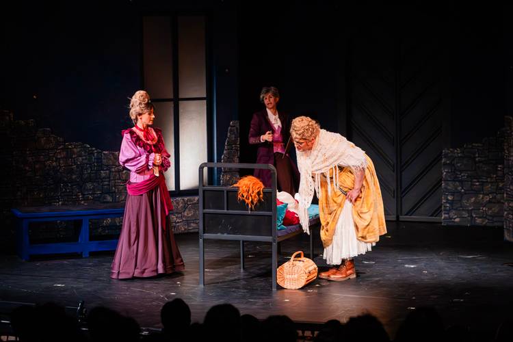 Dracula – A Comedy of Terrors – Drei Personen in einem Theaterstueck auf der Buehne, eine sitzt auf dem Bett, uebrige stehend, alle kostuemiert in historischer Kleidung, Korb am Boden.