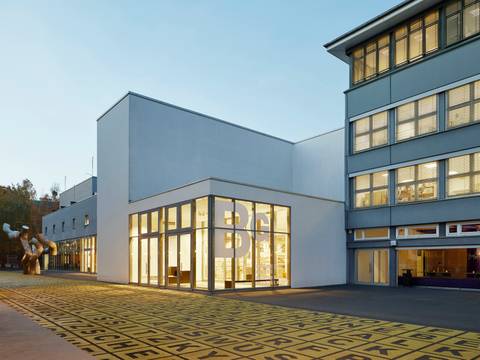 Berlinische Galerie, Außenansicht – Foto: Gebäude mit Flachdach und Glasfront, auf der das Logo der Berlinischen Galerie abgebildet ist. Davor ein Platz mit einer Metallskulptur und Bodenkunstwerk.