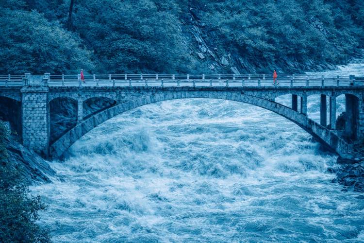 Architecture of Trust 1 – Zwei Personen gehen auf einer Brücken aufeinander zu, die über einen reißenden Fluss führt.