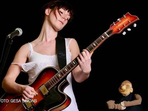 PAUL UND PAULA - EINE LEGENDE – Person spielt E-Gitarre neben Mikrophon. Die Person trägt ein Trägerkleid. Daneben eine Puppe in schwarzem Hemd. Text: FOTO: GESA SIMONS.