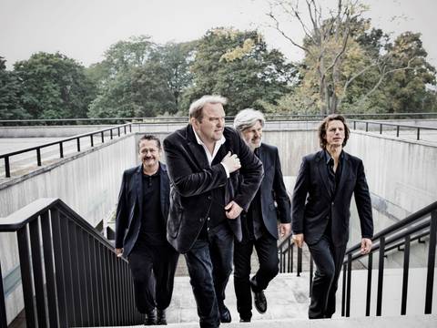 Gustav Peter Wöhler Band: LIVE ON STAGE – Vier Personen in dunklen Anzügen gehen im Freien eine Treppe hinauf. Im Hintergrund sind Bäume und ein bewölkter Himmel sichtbar.