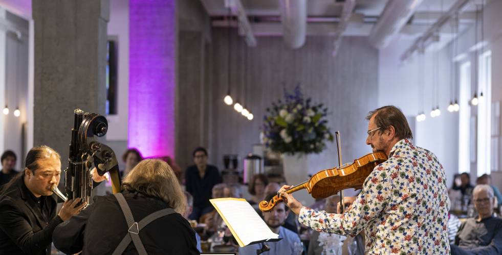 Musiker sind umringt von Zuschauern, die an Tischen mit Getränken sitzen