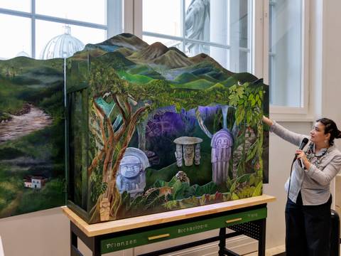Yorleny Cardozo Peña vor ihrer künstlerischen Intervention "Die Stimme der Berge / La voz de la Montaña" – Eine Frau zeigt ein kunstvolles Diorama mit einer Landschaft und mystischen Elementen in einem hellen Raum.