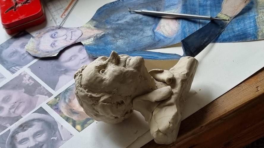 Astrid Lindgren – Ton-Skulptur eines Gesichts auf einem Tisch mit farbiger Zeichnung und ausgedruckten Porträts im Hintergrund.