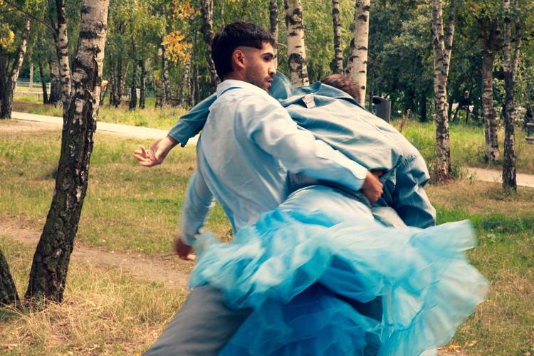 Person trägt eine andere durch den Wald. Beide tragen blaue Kleidung, die untere ein fließendes blaues Kleid. Birken im Hintergrund.