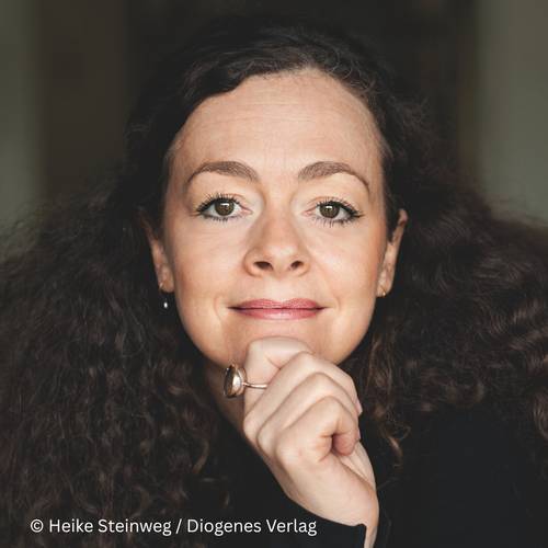 Shelly Kupferberg – Person mit lockigem Haar lächelt sanft, stützt Kinn auf Hand mit Schmuckring auf. Text: © Heike Steinweg / Diogenes Verlag.