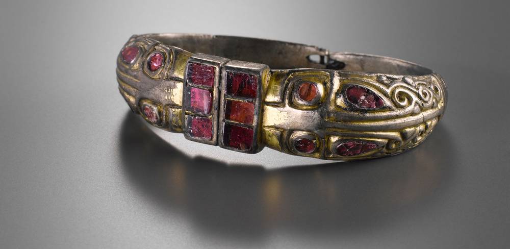 Armring mit Tierkopfenden, Marchélepot, Frankreich, um 500 n. Chr. – Silberarmreif mit roten Steinen und goldenem Muster, verziert mit eingravierten Details auf grauem Hintergrund.