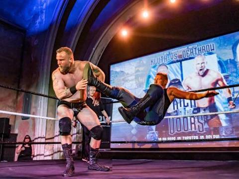 Odeum Pro Wrestling – Zwei Personen ringen im Ring, eine Person in schwarzer Hose hebt eine andere Person. Hintergrund: Projektion mit Text "Kluth vs Oberhau".