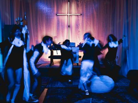 Foto: Michał Wojtarowicz – Fünf Personen in Bewegung vor einem blau beleuchteten Raum mit großem leuchtendem Kreuz an der Wand.