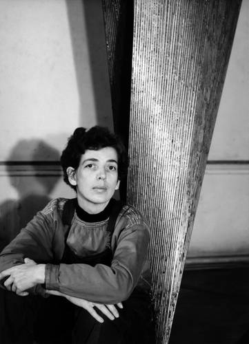 Brigitte Meier-Denninghoff – Schwarz-weiß-Foto: Brigitte Meier-Denninghoff sitzt neben einer, zum Teil abgebildeten, silbernen Skulptur am Boden. Die Arme leicht übereinander auf die Knie gestützt, blickt sie direkt in die Kamera.