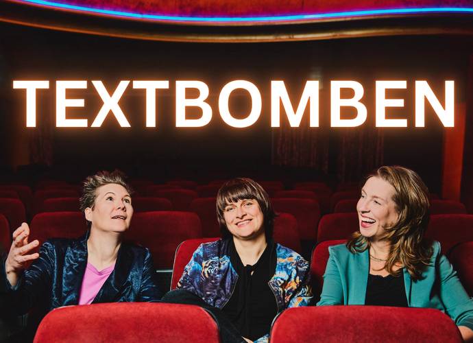 Die Textbomben – Drei lachende Personen in einem Theater mit roten Sitzen, darüber leuchtender Schriftzug "TEXTBOMBEN".