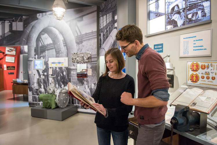 Dauerausstellung "Alltag in der DDR" – eine Frau und ein Mann betrachten gemeinsam eine Mappe mit Dokumenten aus der Ausstellung "Alltag in der DDR"