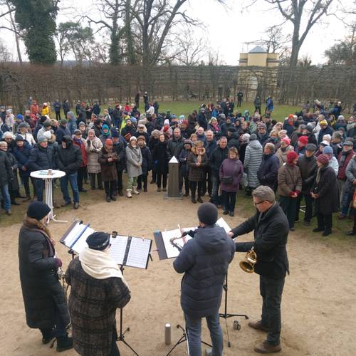 Neujahrskonzert – Blasmusikgruppe mit Notenpulten spielt im Freien vor einer großen Menge von Menschen in Winterkleidung in einem Park.