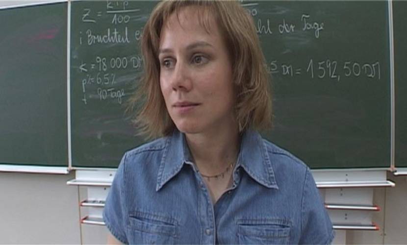 © Komplizen Film – Lehrerin in blauem Hemd vor Tafel