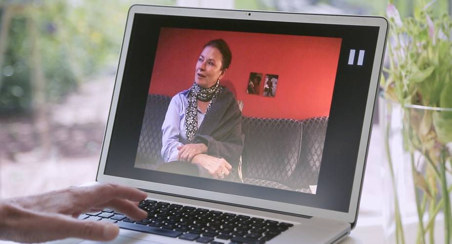 ›Er Sie Ich‹ © Carlotta Kittel – Eine Frau auf einem Laptop-Bildschirm, die mit jemandem spricht, während sie auf einer Couch sitzt.