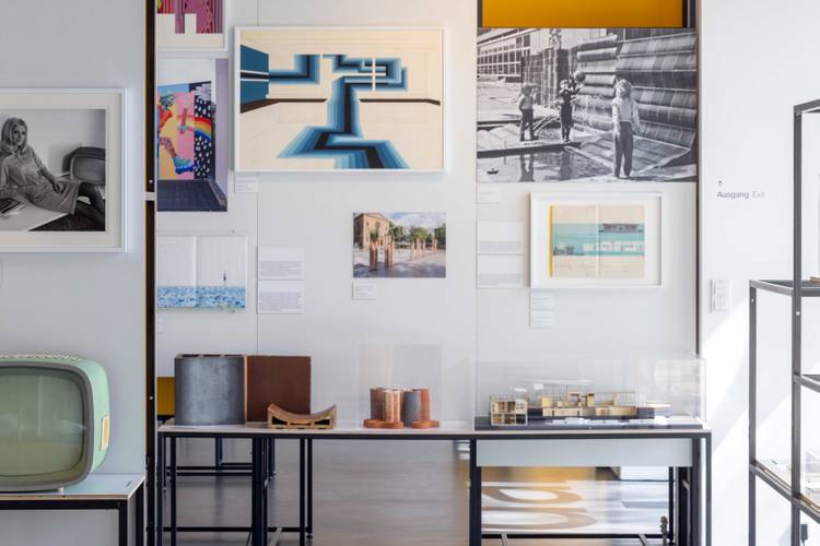 Ausstellungsansicht „Gestalten für Berlin. Design aus der Kunsthochschule Berlin-Weißensee“ – Ausstellungsansicht mit Architekturmodellen, Fotografien und Grafiken an einer weißen Wand neben einem historischen Fernsehgerät
