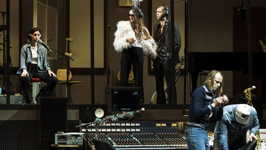 Stereophonic – Fünf Personen in einem Tonstudio, zwei sitzend, drei stehend mit Kopfhörern. Eine Person trägt ein flauschiges Kostüm. Mischpult im Vordergrund.