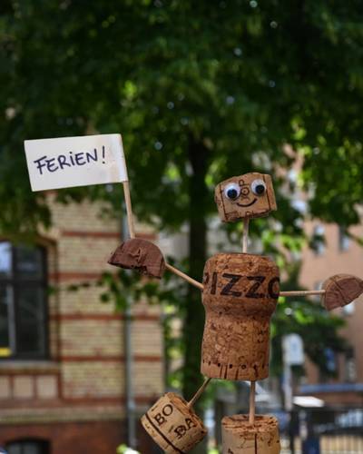 Mit Korkmännchen basteln wir uns durch die Geschichte der Straßennamen. – Ein selbstgebasteltes Korkmännchen schwenkt eine Fahne mit der Aufschrift "Ferien!".