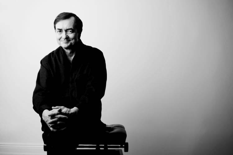 Pierre-Laurent Aimard – Mann sitzt den Betrachtenden zugewandt vor weißem Hintergrund auf Klavierhocker