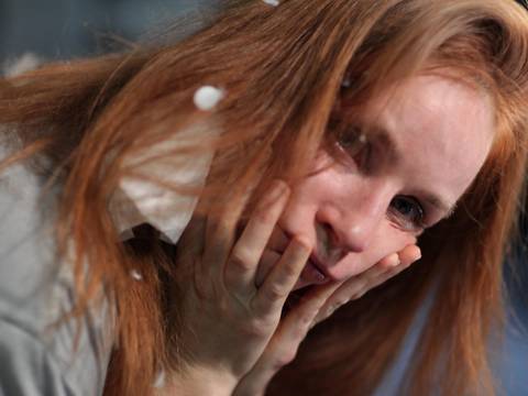  – Person mit roten langen Haaren haelt Gesicht mit beiden Haenden. Einige Schaumflocken sind im Haar und auf Kleidung sichtbar.