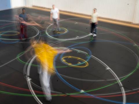 Gla55. 10 movements to the music of Philip Glass – Mehrere Personen stehen oder bewegen sich in einem Probenraum, um sie herum sind bunte Kreise.