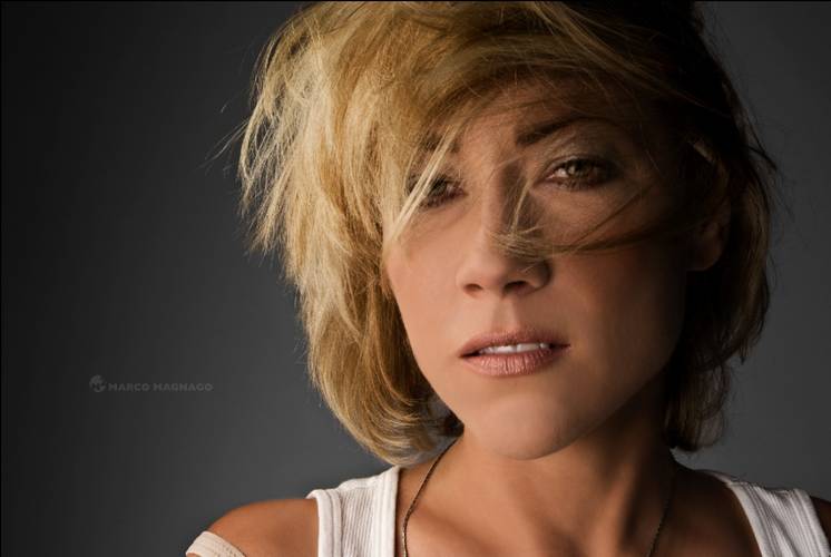 Shannon Callahan – Person mit kurzem blondem Haar, leicht zerzaust, blickt in die Kamera. Weiße Kleidung. Text: Marco Magnago.