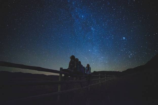 Zu sehen ist ein dunkler Nachthimmel mit leuchtenden Sternen und Kindern, die in den Himmel schauen, passend zur Veranstaltung in der Archenhold-Sternwarte der Stiftung Planetarium Berlin.