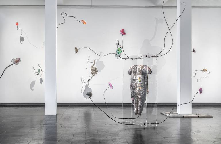 Mariechen Danz, Clouded in Veins, 2021 – Blick in einen Ausstellungsraum, in dem eine Installation aus dünnen, gebogenen Metallstangen zu sehen ist, an die bunte Objekte angebracht sind.