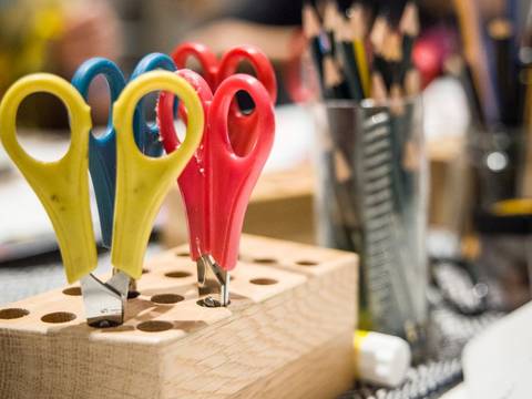  – Foto: Nahaufnahme von Scheren in einem Holz-Ständer. Der Hintergrund zeigt Bleistifte in einem Glas.