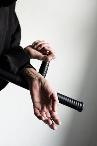 SAN PAOLO. Das Martyrium von Pasolini – Nahaufnahme von Händen, die ein Katana mit schwarzem Griff halten, gekreuzt vor einem neutralen Hintergrund.