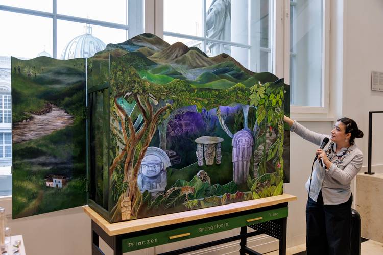 Yorleny Cardozo Peña vor ihrer künstlerischen Intervention "Die Stimme der Berge / La voz de la Montaña" – Eine Frau zeigt ein kunstvolles Diorama mit einer Landschaft und mystischen Elementen in einem hellen Raum.