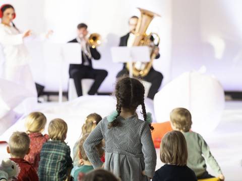  – Kinder im Publikum, zwei Musiker spielen Musik, zwei Frauen in weißen Anzügen