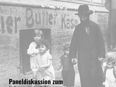 Scheunenviertelpogrom 1923 Gedenktag – Schwarz-Weiß-Foto: Person mit Vollbart und Hut führt auf Gehweg vier Kinder an der Hand. An Ziegelwand steht "Tier Butter Käse". Text: "Paneldiskussion zum