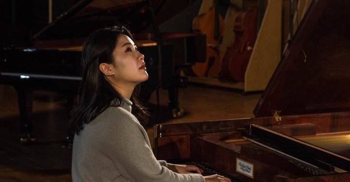 Hyunji Kim – Person an einem Flügel sitzend, spielt Klavier. Im Hintergrund weitere Musikinstrumente.