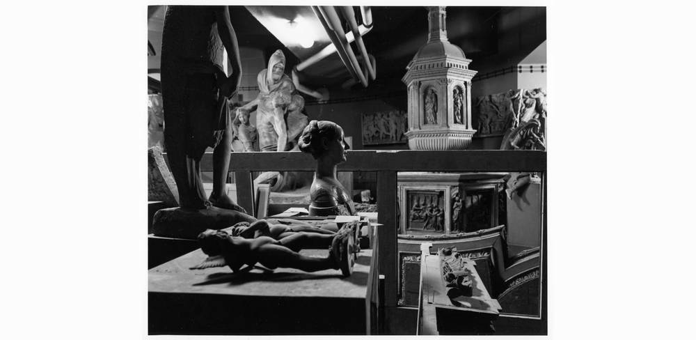 Ein demontierter Abguss des Taufbeckens im Dachgeschoss des Bode-Museums, 1980er Jahre – Schwarz-Weiß-Fotografie von Gipsabgüssen antiker Statuen, Reliefs und Architekturmodell in einem Museum. Skulpturen in verschiedenen Größen und Positionen.