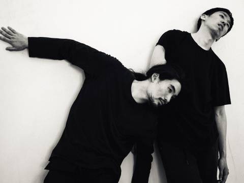 LEAR SHADOW PLAY – Zwei Personen in schwarzer Kleidung lehnen aneinander, eine mit ausgestrecktem Arm an der Wand. Schwarz-weißes Foto.