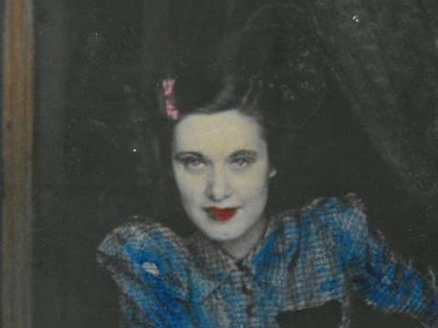 Willi Ruge, Elly Ruge, Detail, um 1947, Silbergelatinepapier koloriert – Schwarzweiß-Fotografie: Eine Person im blauen karierten Hemd, roten Lippenstift tragend, schaut direkt in die Kamera, mit einem dunklen Hintergrund.