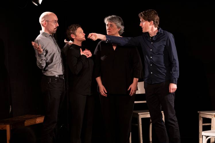 Theater ohne Probe TOP – Vier Personen auf einer Bühne in schwarzer Kleidung. Eine Person zeigt mit dem Finger auf eine andere, alle blicken konzentriert.