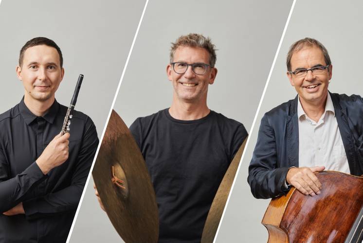Jan Schlichte, Egor Egorkin und Sebastian Krunnies – Drei Personen stehen nebeneinander, eine mit Querfloete, eine mit Becken, eine mit Kontrabass. Studiofotografie mit neutralem Hintergrund.